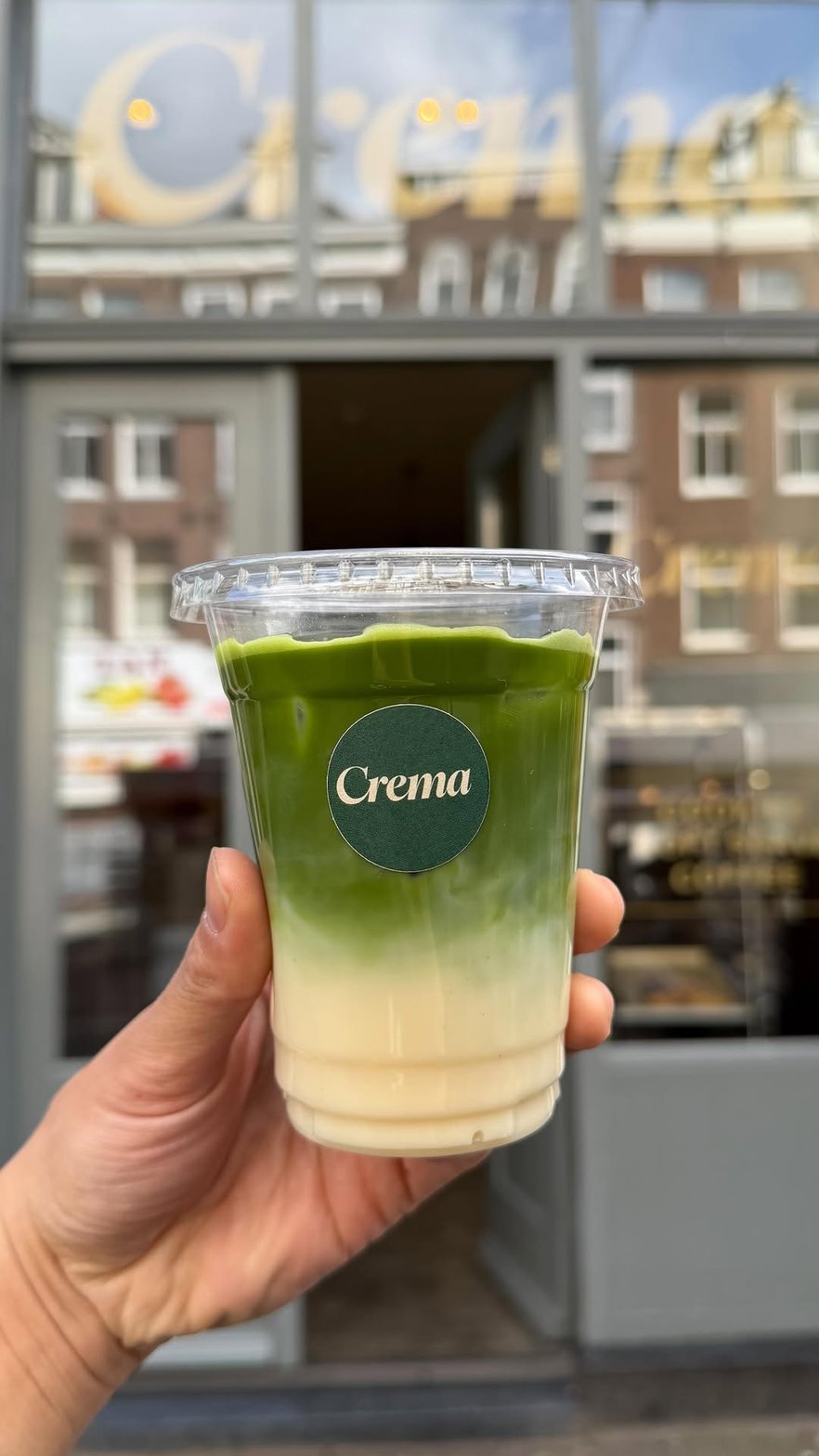 Iced matcha latte from Crema in front of the green storefront with cream wordmark