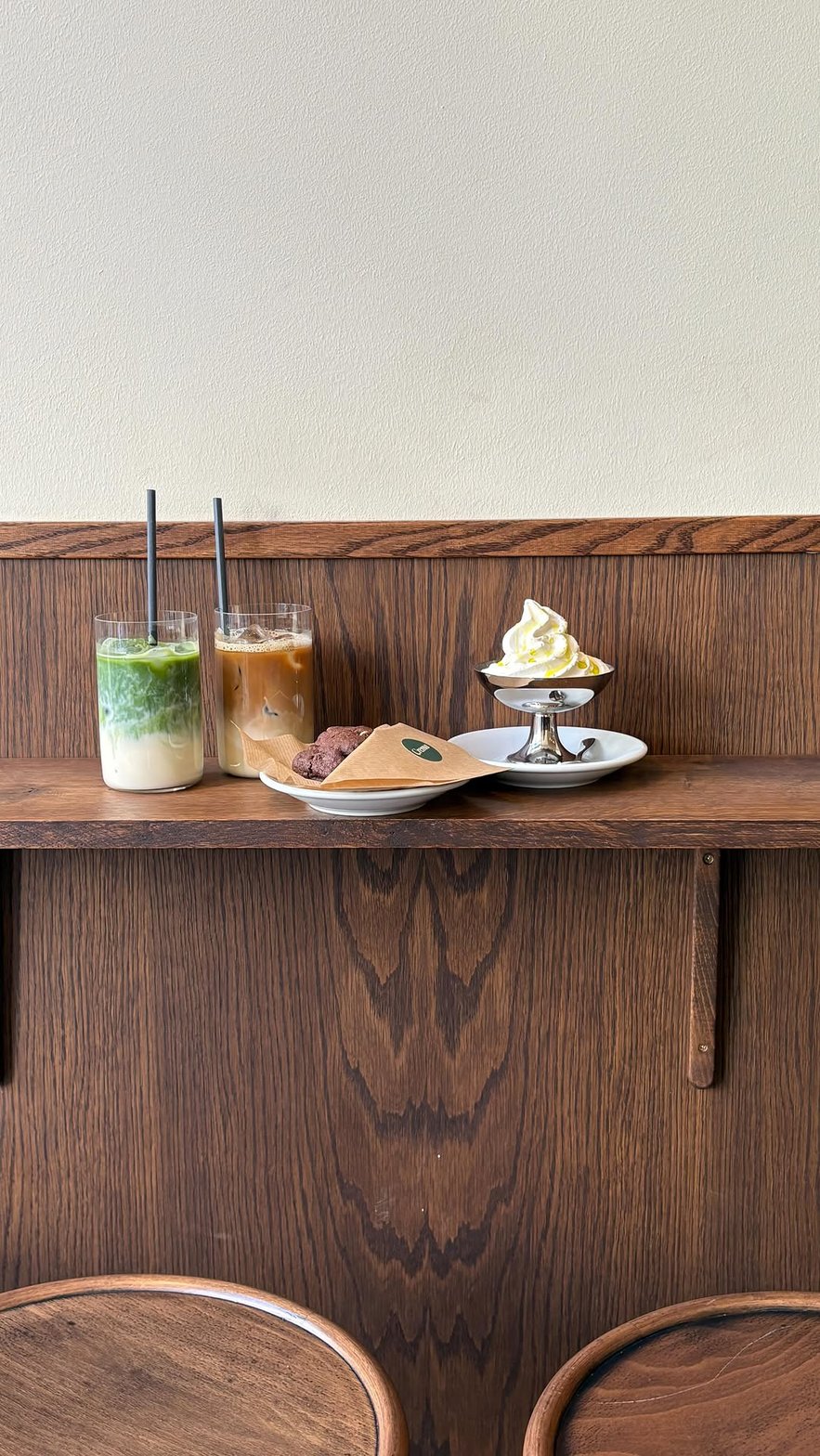 Iced matcha latte, iced coffee, a cookie and soft serve on the warm oak counter at Crema
